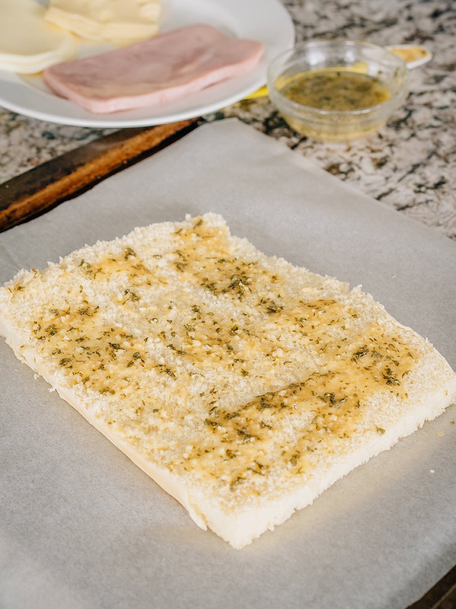 La partie inférieure des petits pains hawaïens badigeonnée du mélange de beurre pour les mini-sandwichs au jambon et au fromage.