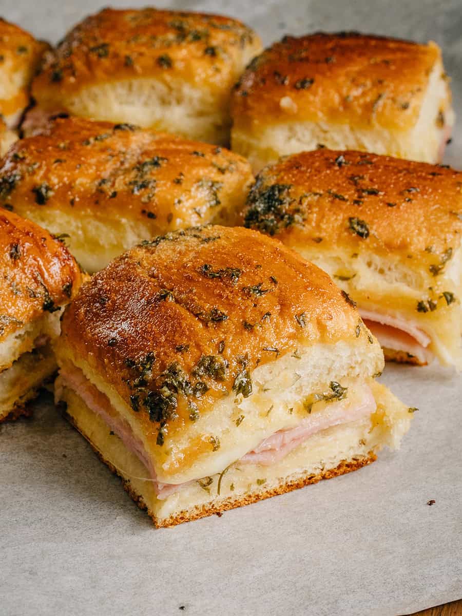 Mini-sandwichs au jambon et au fromage tout juste sortis du four. Fromage fondant et jambon délicieux sur des petits pains hawaïens grillés badigeonnés d'un mélange de beurre savoureux !