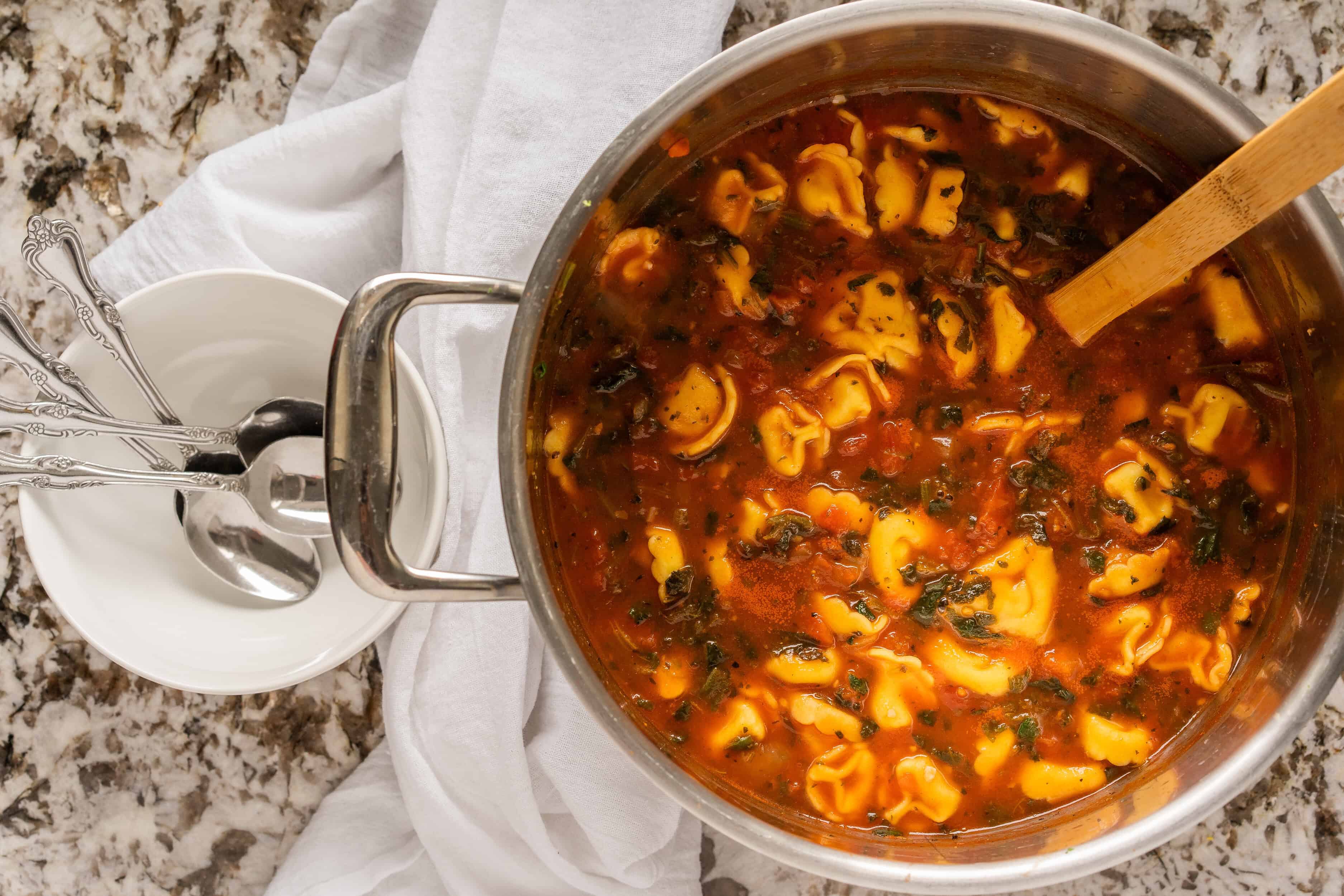 Aperçu de la soupe aux tortellini aux épinards dans une grande casserole avec un bol et des cuillères à gauche.