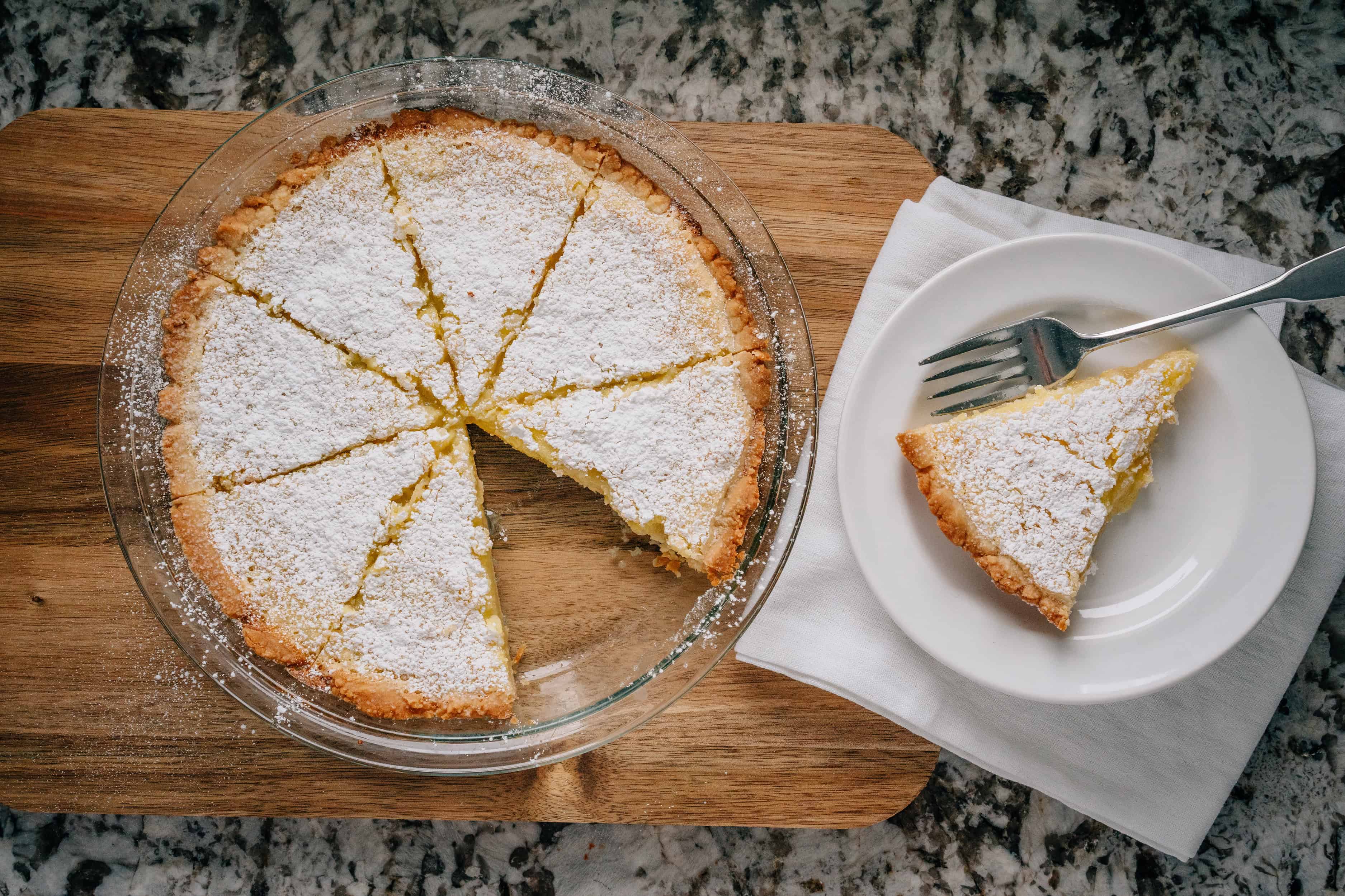 Vue d'ensemble d'une tarte au citron crémeuse saupoudrée de sucre glace dans le moule et sur une assiette.