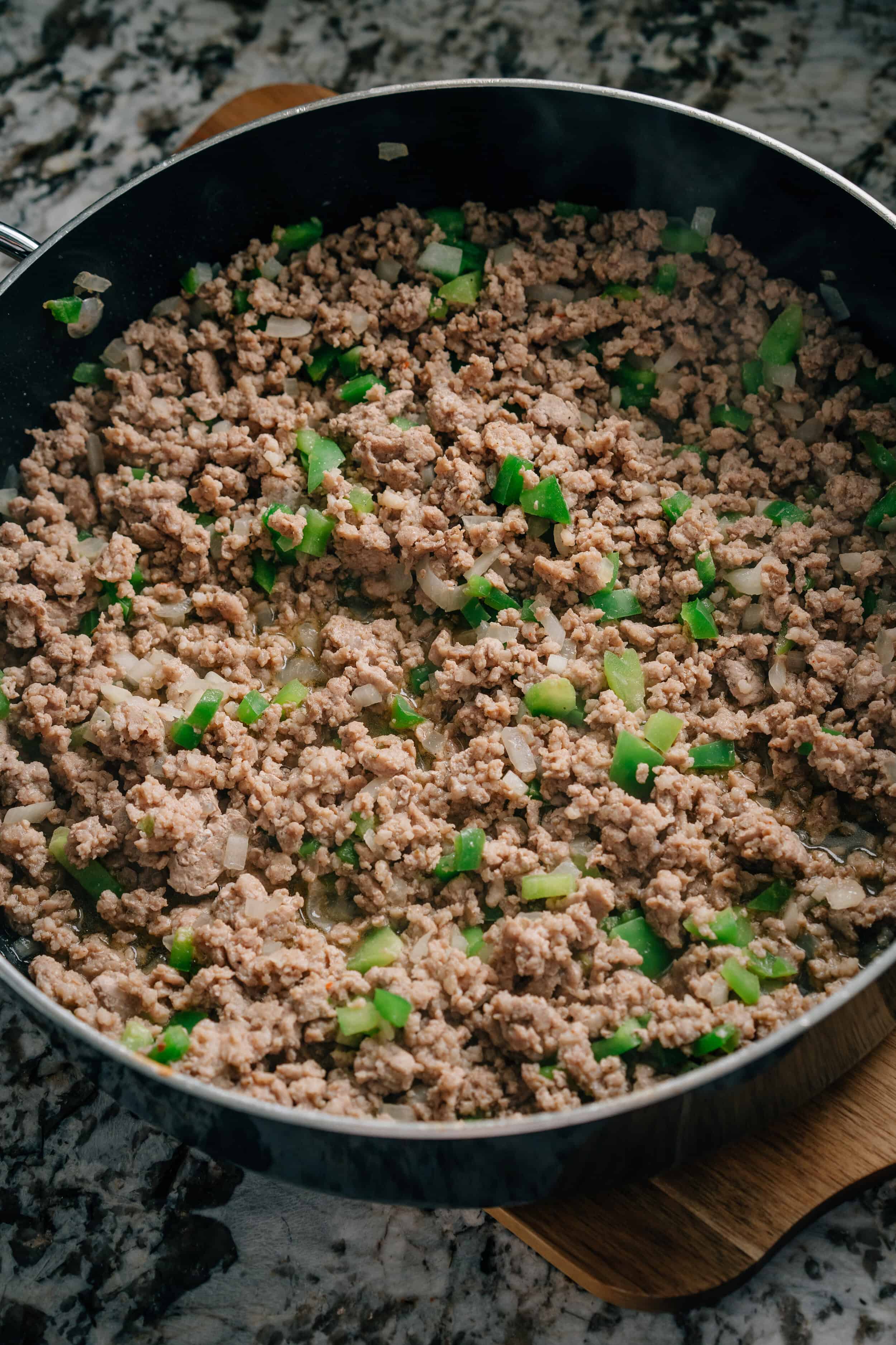 Saucisse dorée, poivrons verts et oignon dans une poêle. Partie de la garniture pour un gâteau de petit déjeuner facile.