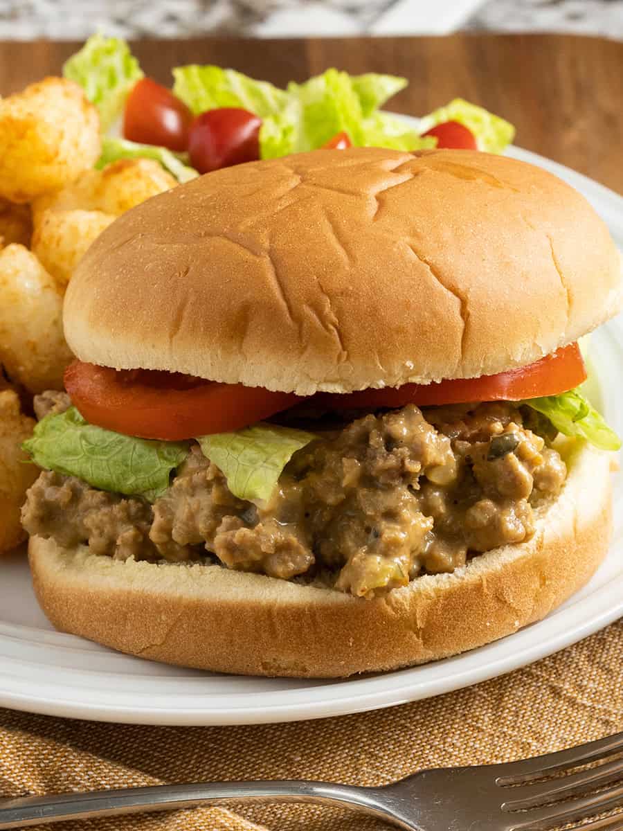 Un cheeseburger au crockpot garni de laitue et de tomate sur un pain, servi avec des tater tots et une salade !