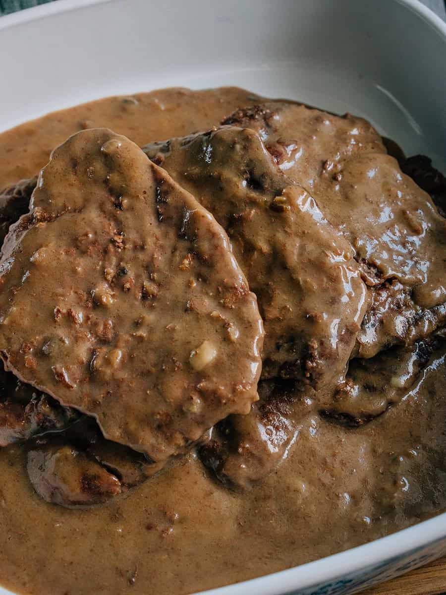 Une pile de steaks en cube dans un plat de service couverts d'une délicieuse sauce à base de crème de champignons et de mélange de soupe à l'oignon. Miam !