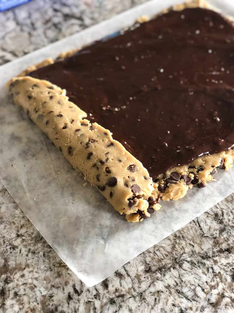 Une feuille de pâte à cookies avec de la pâte à brownie dessus en train d'être roulée d'un côté.