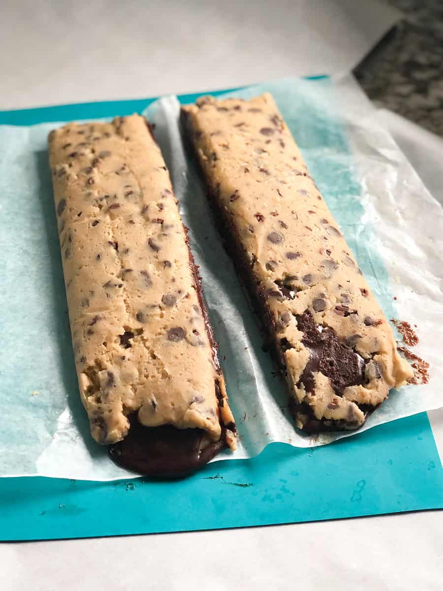 La pâte à cookies congelée et la pâte à brownie roulées ensemble, coupées en deux boudins.