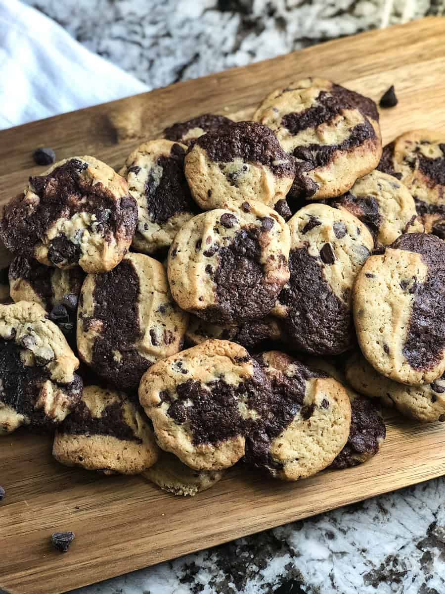 Un tas de délicieux Cookies Brookie sur une planche à découper avec des pépites de chocolat éparpillées devant, vue grand angle.