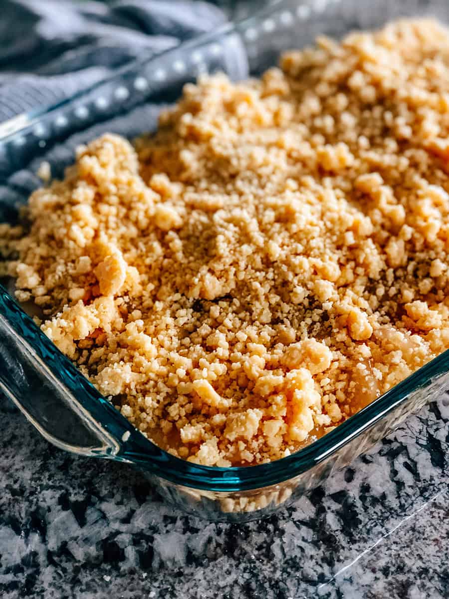 Le crumble de beurre et de mélange à gâteau jaune ajouté au plat sur la garniture de tarte aux pommes et le sirop de caramel.