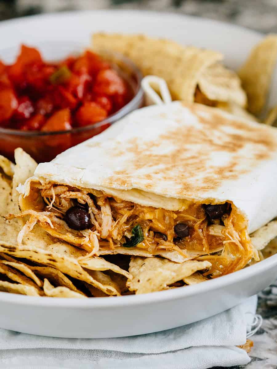 Un wrap au poulet du sud-ouest croustillant avec quelques bouchées prises, posé sur un lit de chips tortilla avec de la salsa en arrière-plan.