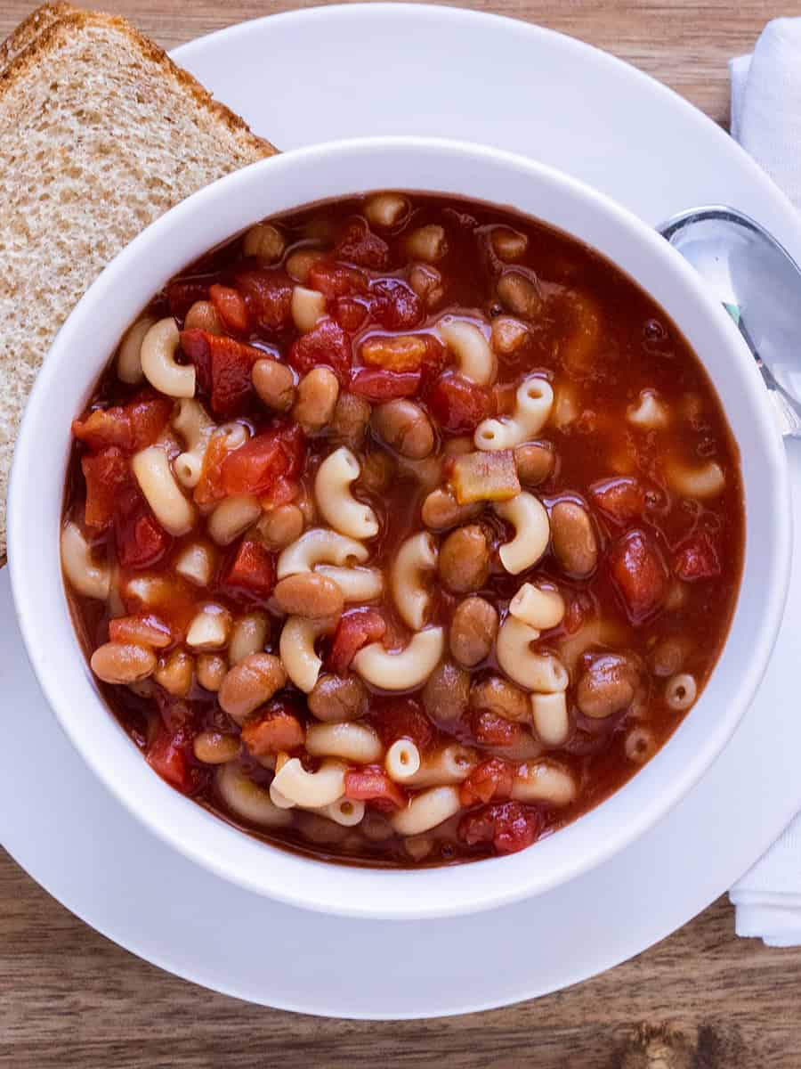 Soupe aux haricots cuits et aux macaronis dans un bol blanc avec du pain beurré sur le côté.