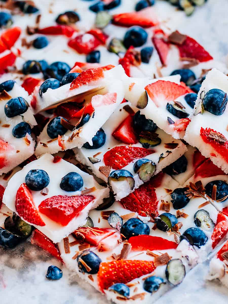 Une pile de barres de yaourt glacé avec des fraises et des myrtilles sur du papier sulfurisé.