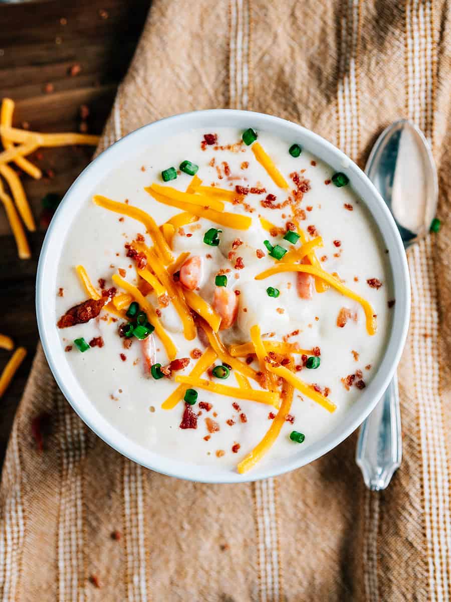 Vue d'ensemble de la soupe de pommes de terre au fromage à la crème dans un bol garnie de morceaux de bacon, de fromage cheddar râpé et d'oignons verts.