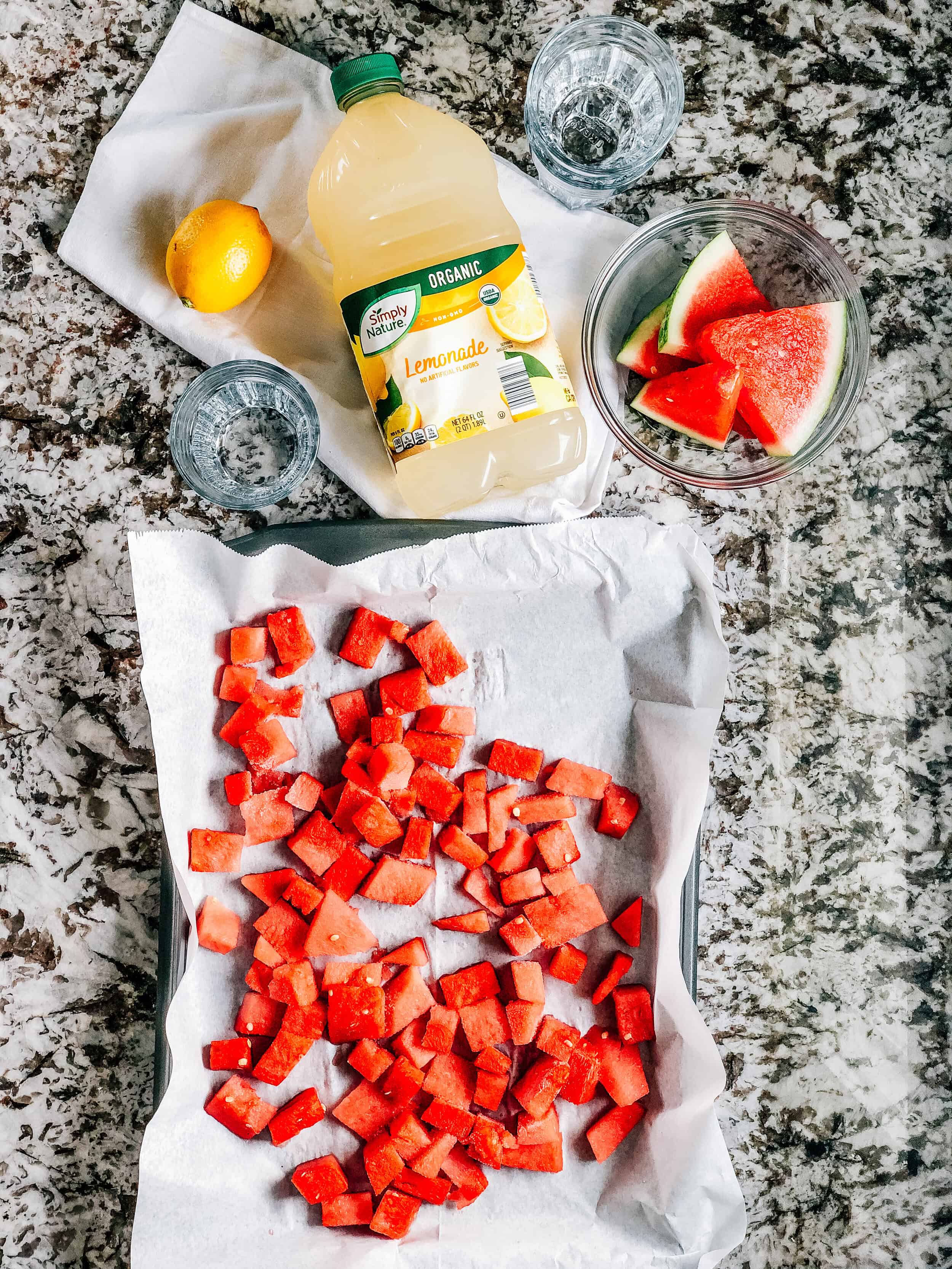 Les ingrédients des slushies à la limonade de pastèque : pastèque congelée et limonade avec un citron et des tranches de pastèque pour garnitures.