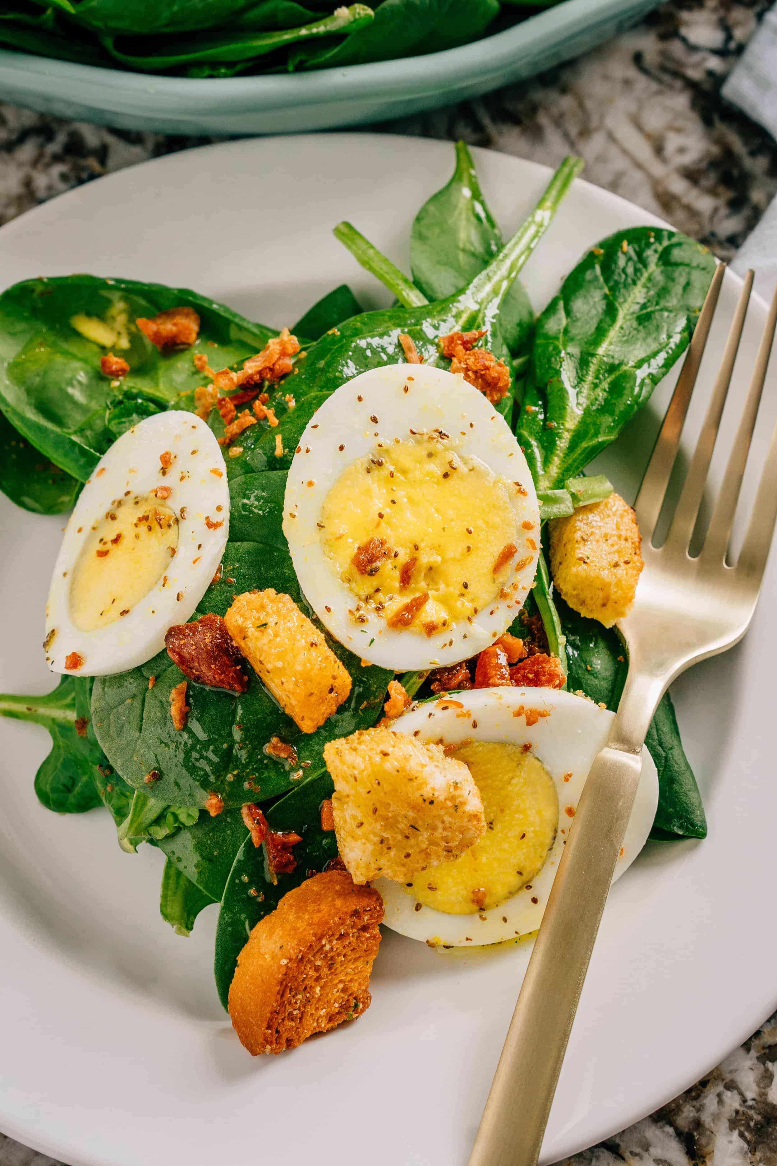 Salade d'épinards terminée. Épinards, œufs, morceaux de bacon et croûtons recouverts d'une vinaigrette maison aigre-douce sur une assiette.