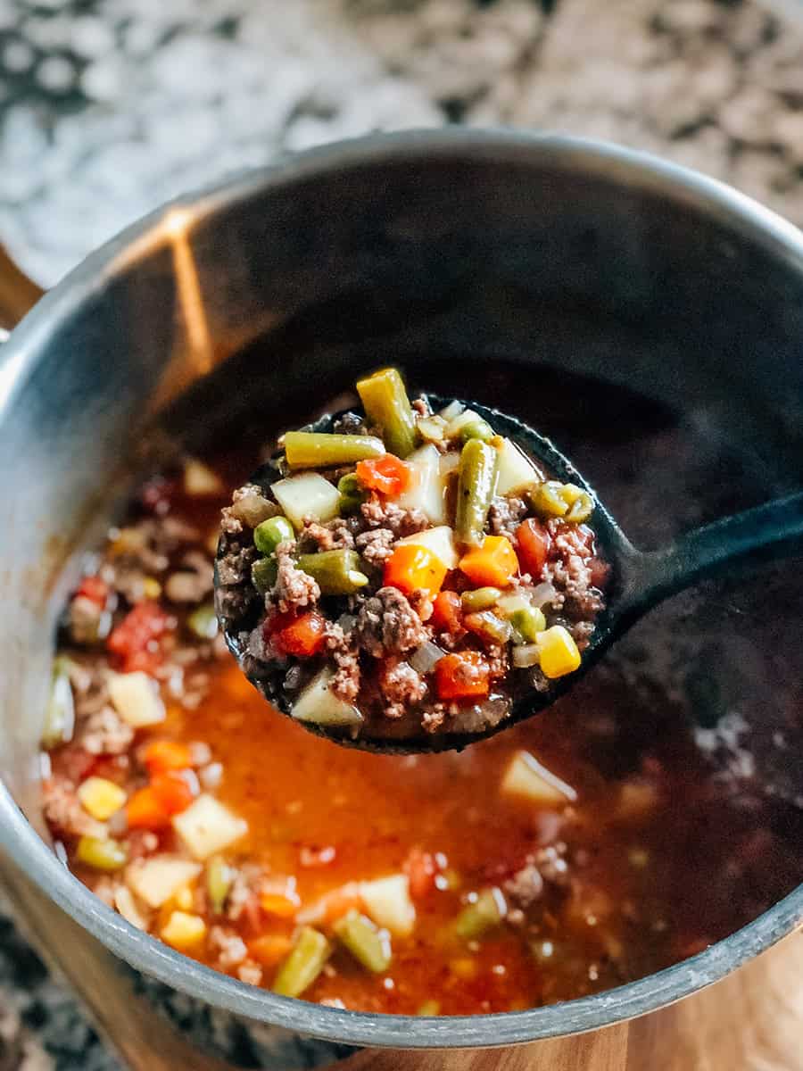 Une louche de soupe de hamburger avec des légumes congelés, chaude et prête à être servie.