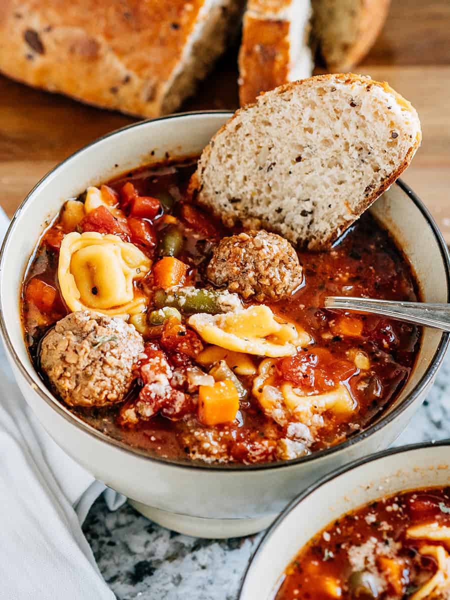 Soupe de boulettes de viande italiennes et de tortellini au fromage facile garnie de fromage parmesan et d'une tranche de pain croustillant. La soupe chaude parfaite !