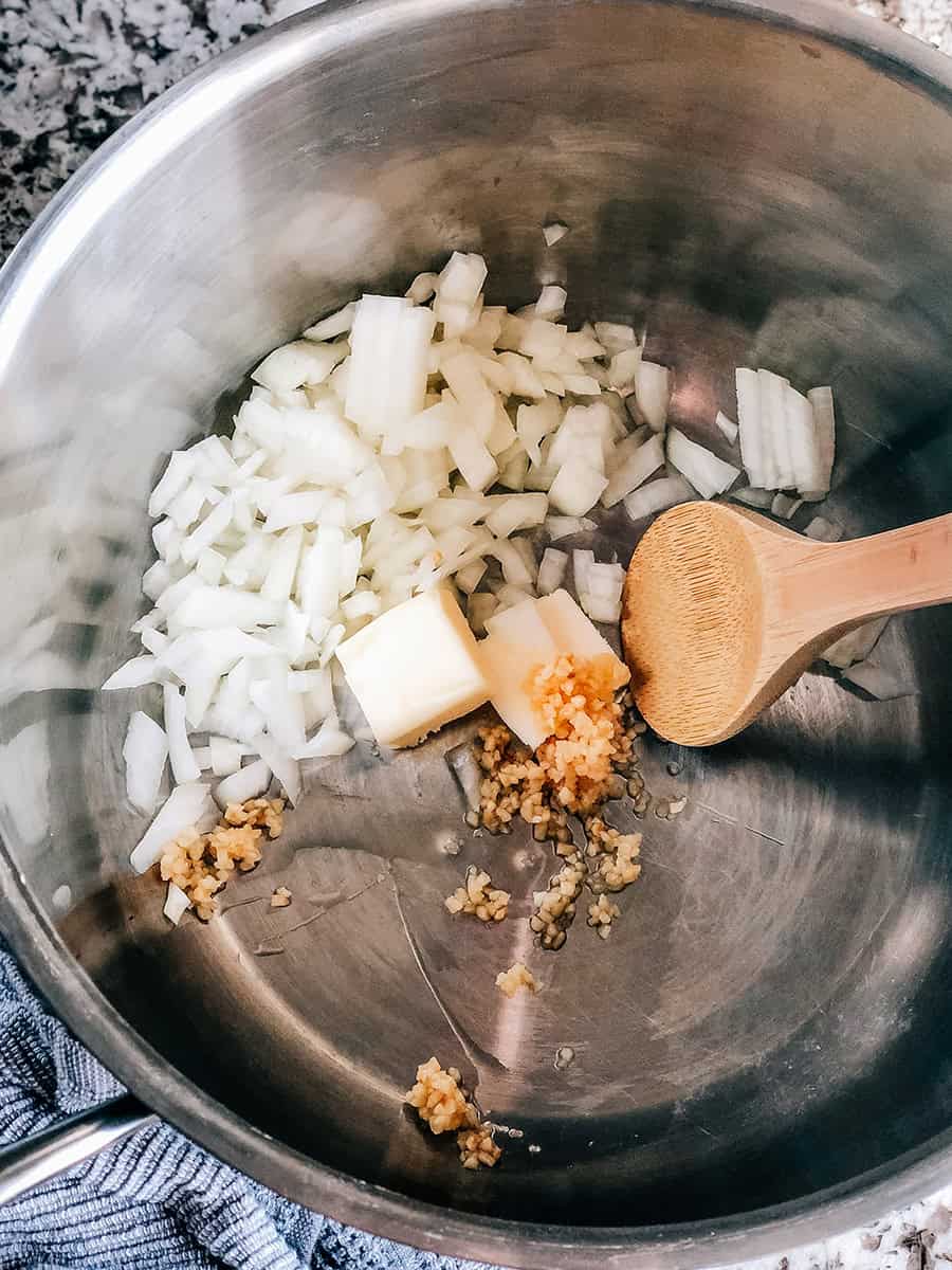 Image de processus de la soupe de boulettes de viande italiennes : Beurre, ail émincé et oignon jaune haché dans une grande casserole.