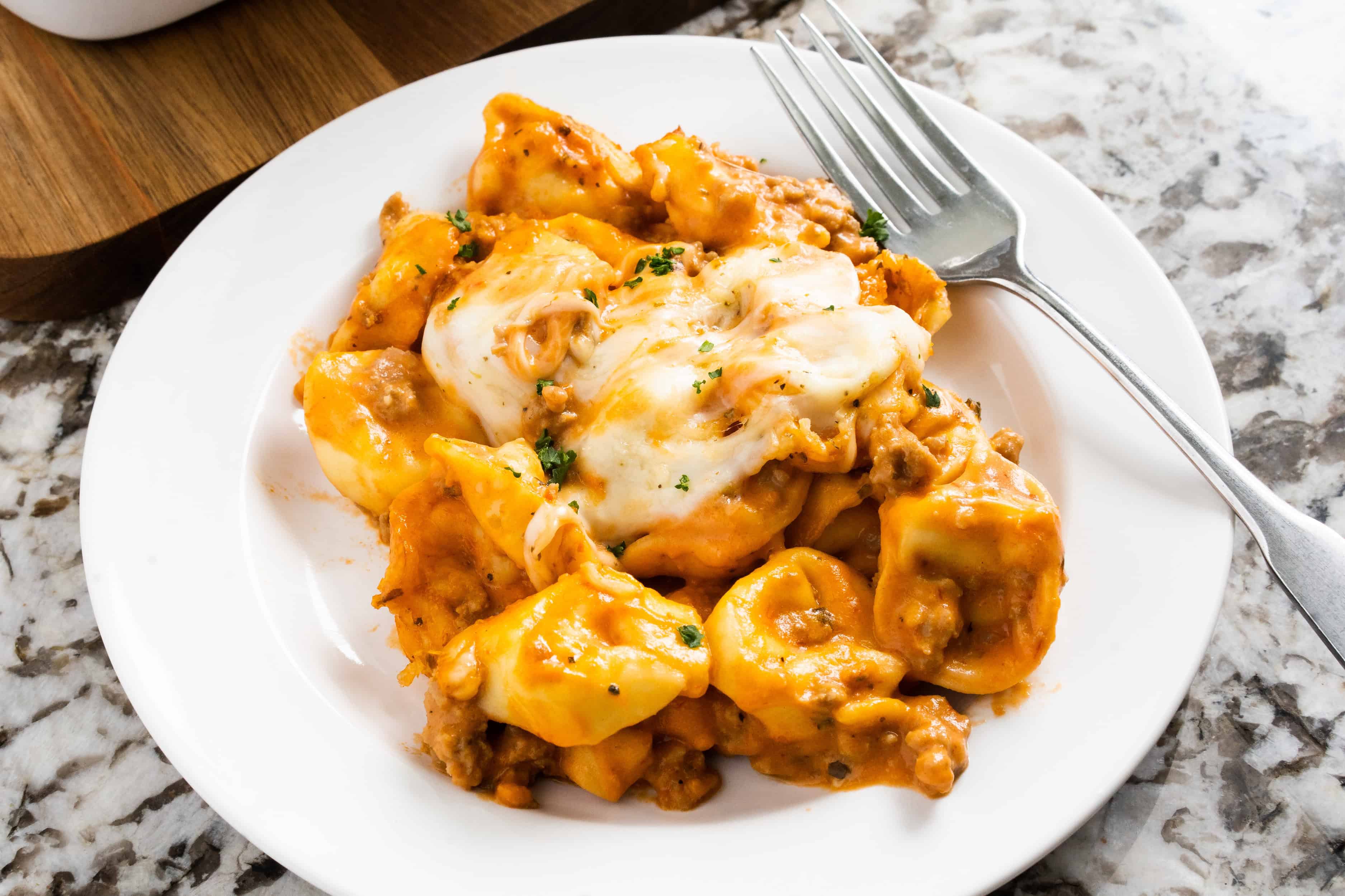 Tortellini crémeux à la saucisse avec garniture de fromage dans une assiette.