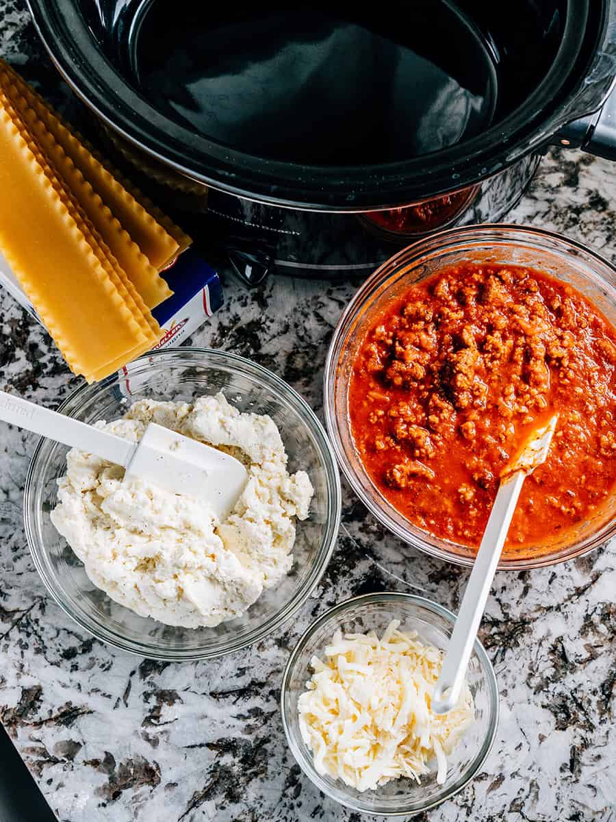 Nouilles à lasagne, sauce à viande, mélange de fromage et topping de fromage tous dans des bols attendant d'être assemblés dans la lasagne la plus facile à la mijoteuse.