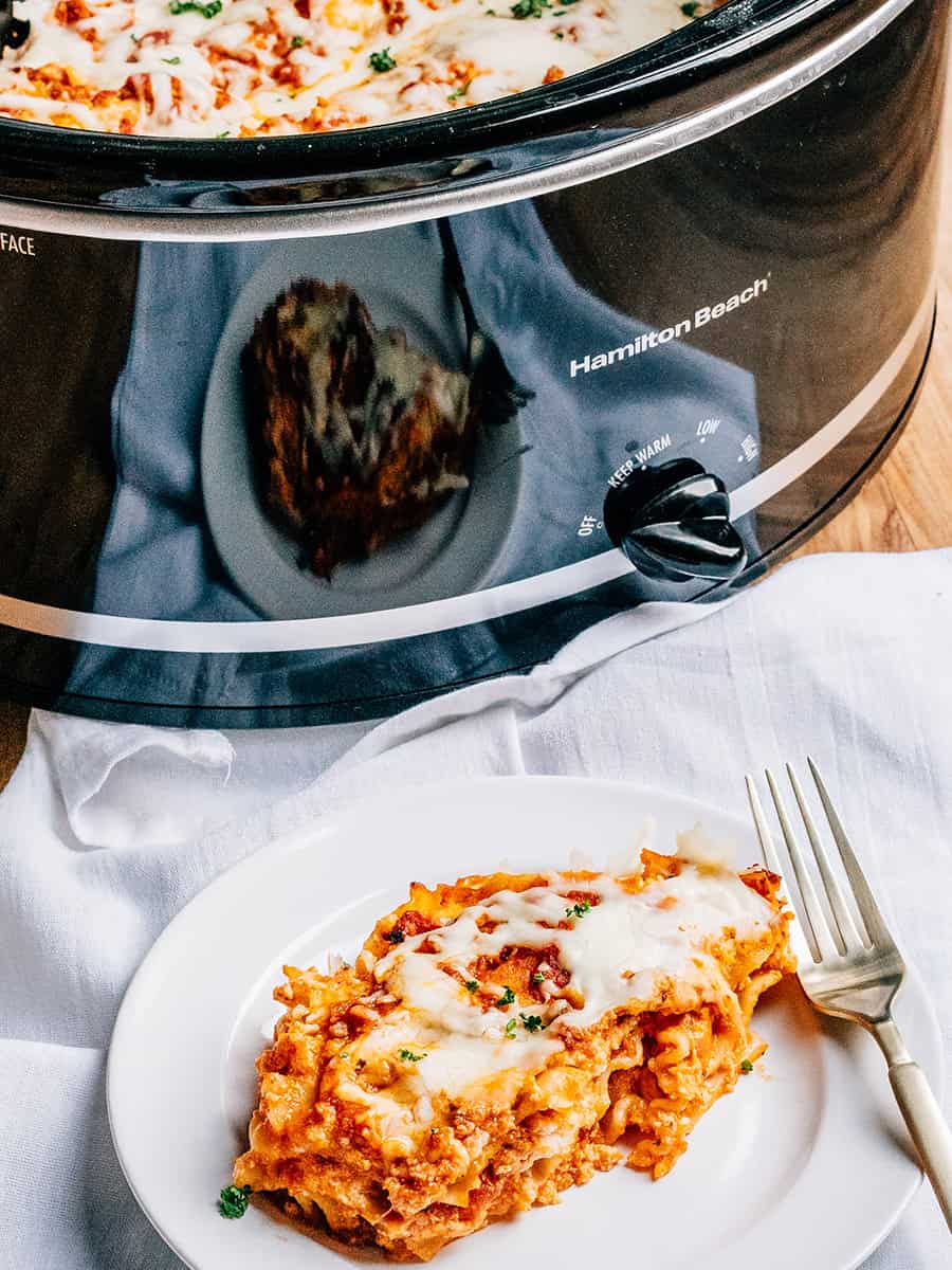 Une portion de lasagne facile à la mijoteuse dressée et prête à être dégustée avec la mijoteuse en arrière-plan.