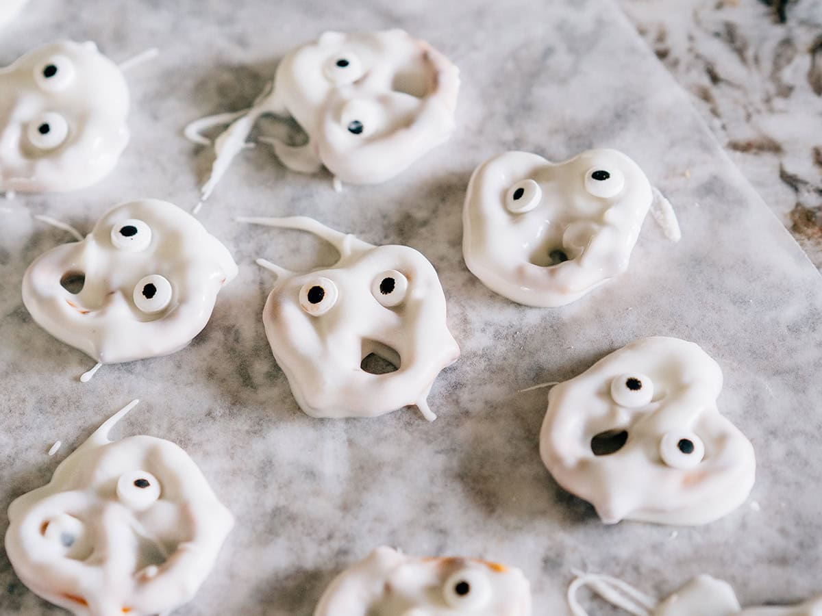 Les visages de fantômes hilarants sont de délicieux bretzels torsadés recouverts de chocolat blanc avec des yeux en bonbons posés sur du papier ciré.