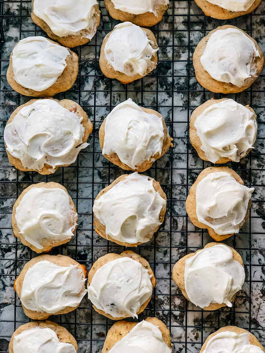 Une douzaine de cookies de courgettes avec glaçage au fromage à la crème sur une grille.