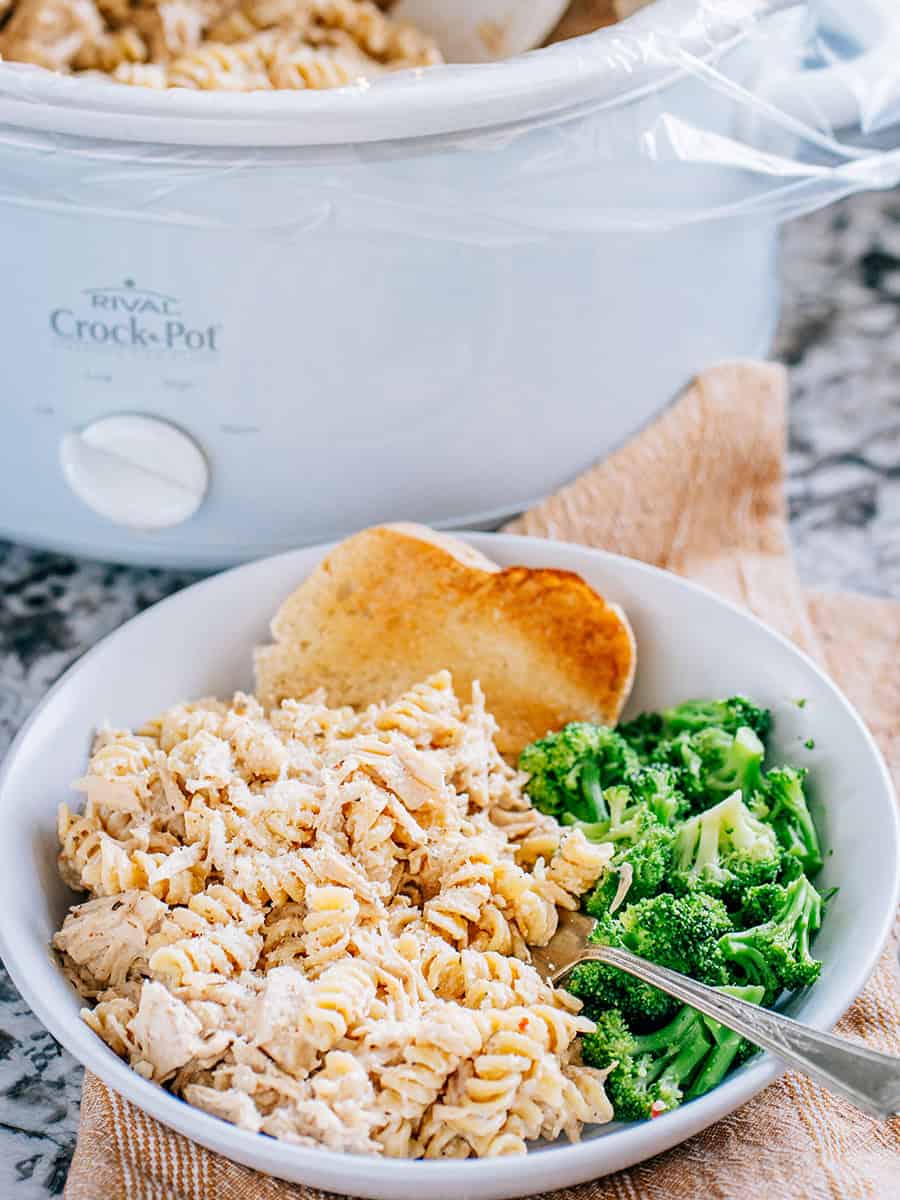 Un plat de pâtes au poulet ail et parmesan dans la mijoteuse, accompagné de brocoli vapeur et de pain à l'ail.