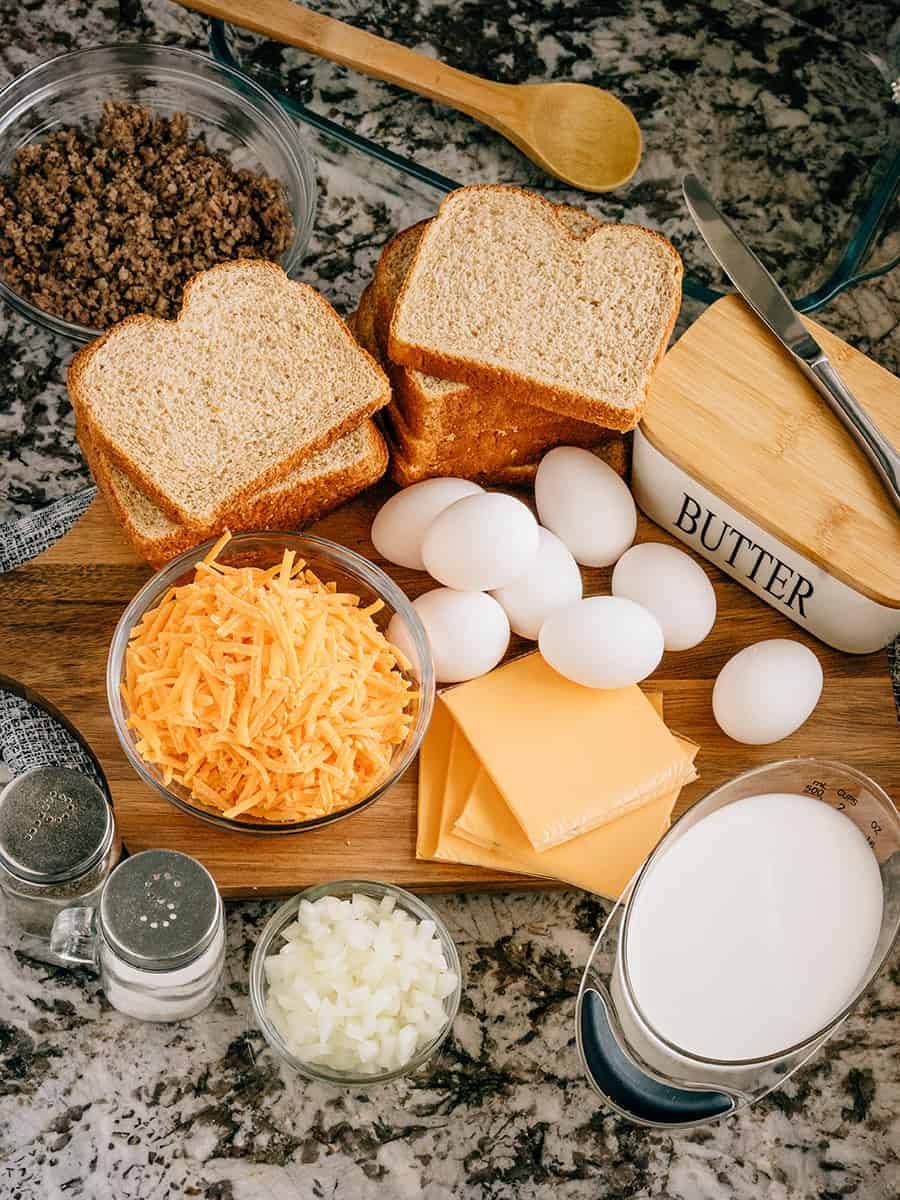 Pain de blé, lait, œufs, fromage, oignons, saucisse de petit-déjeuner dorée et du sel et du poivre sont tous les ingrédients de cette casserole de petit-déjeuner.