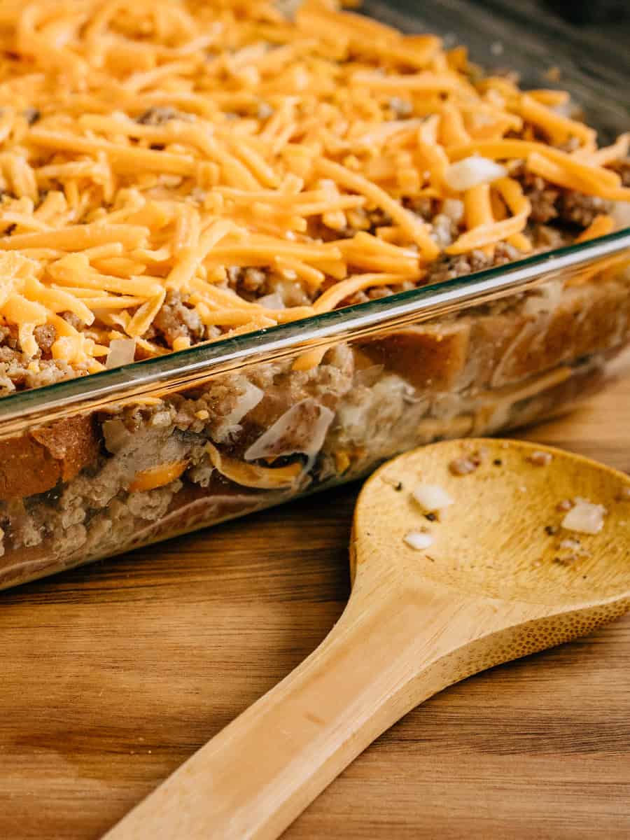 Vue latérale de la casserole de petit-déjeuner préparée montrant les couches de pain, de fromage, de saucisse de petit-déjeuner, d'oignons et de fromage râpé.