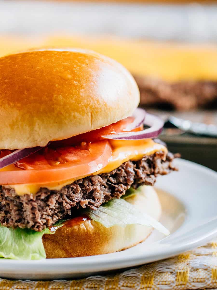 Gros plan d'un hamburger sur une baguette garni de fromage, ketchup, laitue, tomate et oignon rouge.