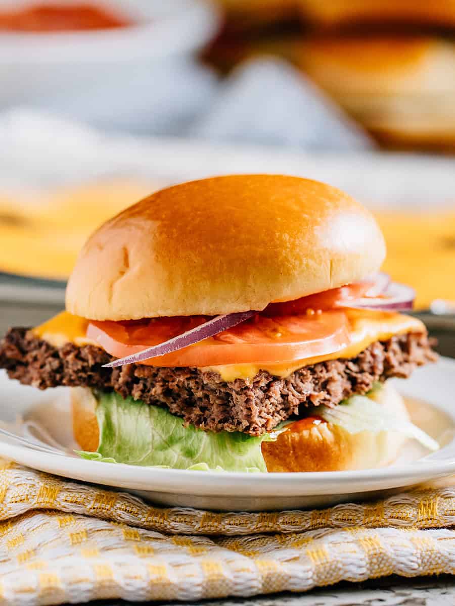 Un cheeseburger cuit au four sur une baguette garni de ketchup, laitue, tomate et oignon rouge.