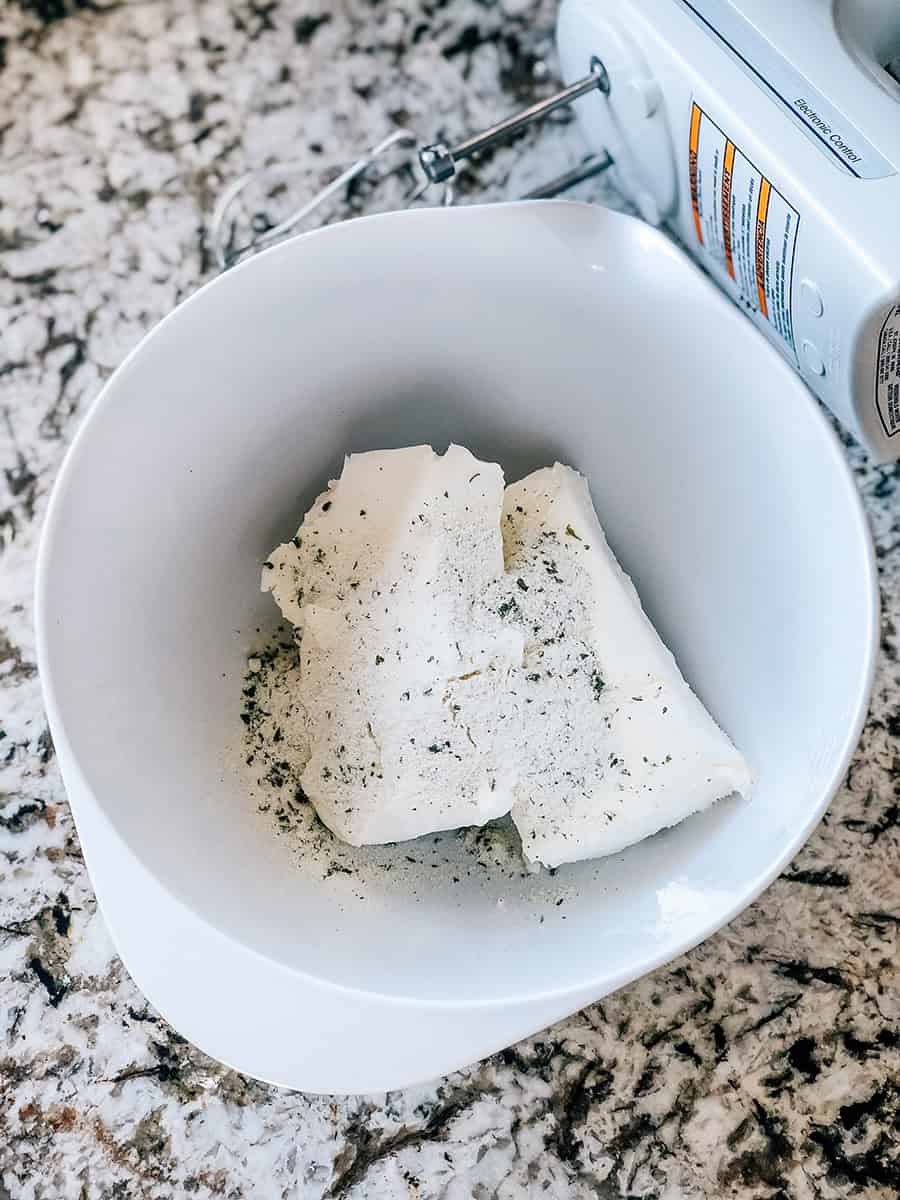 Du fromage à la crème ramolli et un assaisonnement ranch dans un bol, prêts à être mélangés.