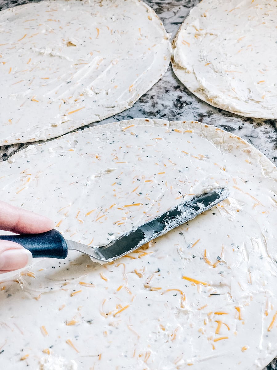 Un couteau à glaçage étalant le mélange de fromage à la crème sur une tortilla de farine.