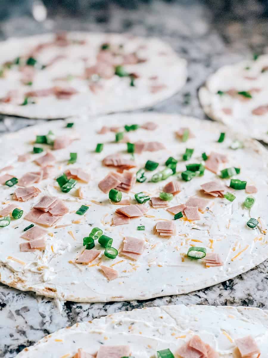 Gros plan montrant le jambon haché et les oignons verts ajoutés sur les tortillas avec le mélange de fromage à la crème.