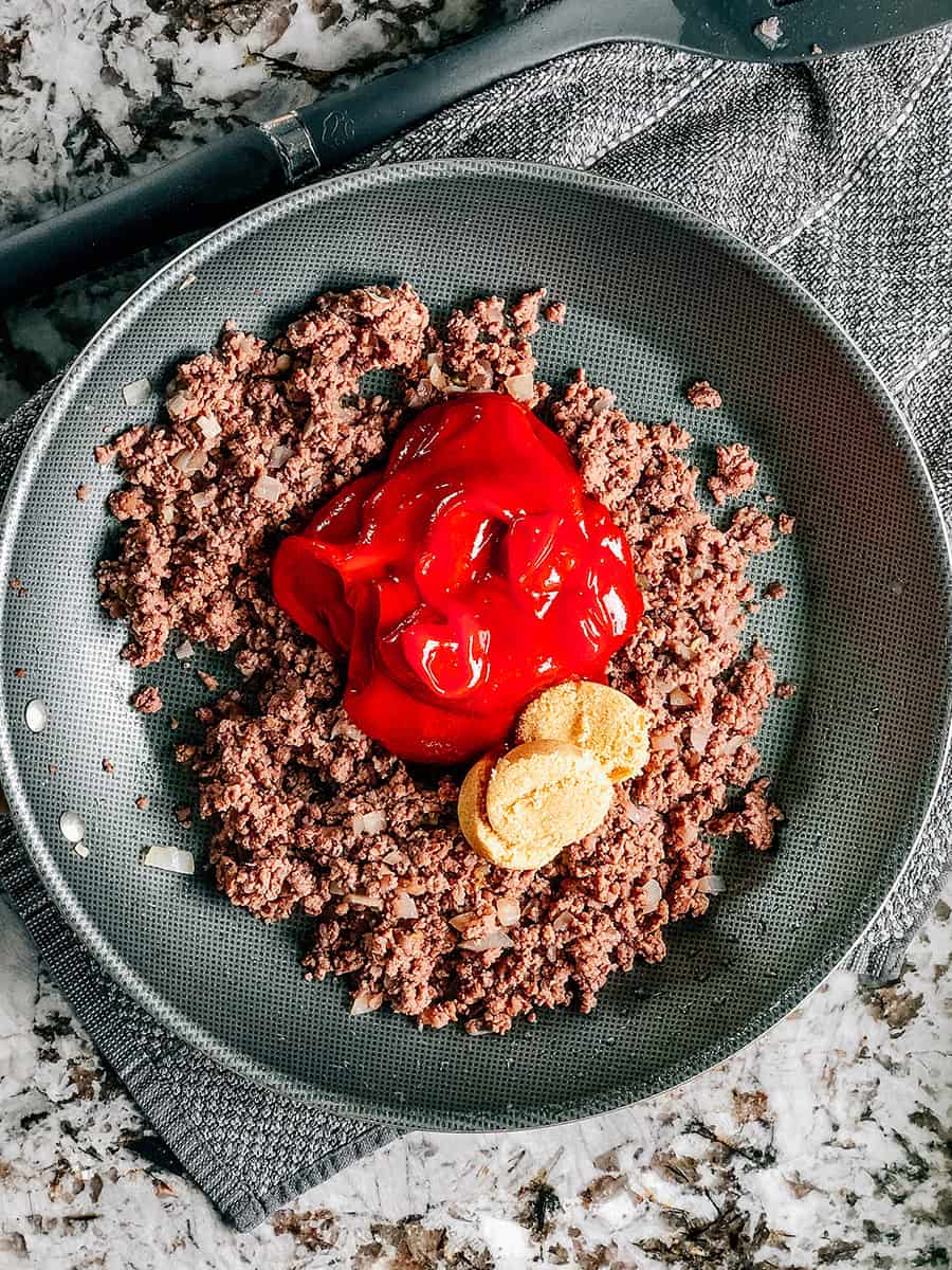 Une poêle avec de la viande hachée dorée, du ketchup et du sucre brun.