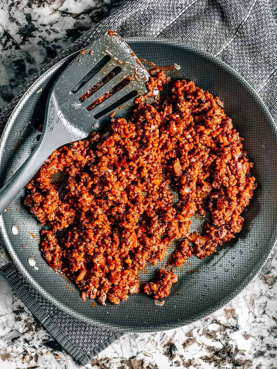 La viande hachée dorée avec des oignons, du ketchup et du sucre brun remués. La première étape pour préparer la casserole de Tater Tot aux Sloppy Joes.