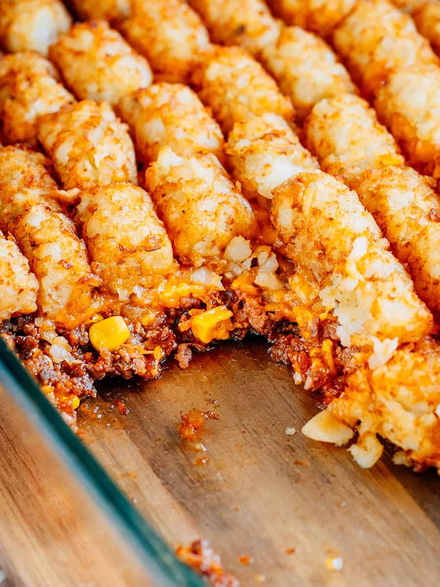 Vue à l'intérieur de la casserole montrant les couches de Sloppy Joe mélangées avec du maïs, du fromage cheddar râpé et des Tater Tots croustillants dorés.