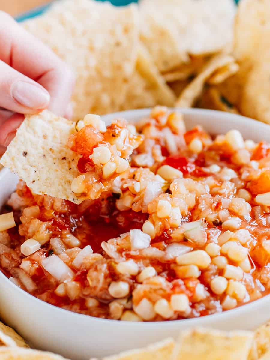 Une chip tortilla trempée dans la salsa ananas maïs, montrant la salsa épaisse, le maïs, l'ananas et l'oignon doux haché.