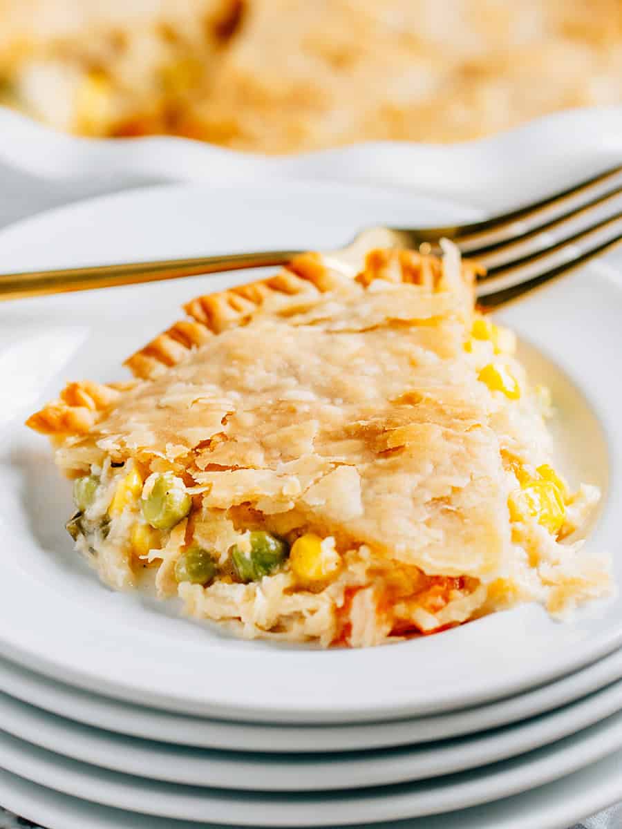 A slice of chicken pot pie plated with vegetables, shredded chicken, and cheese pouring out the sides.