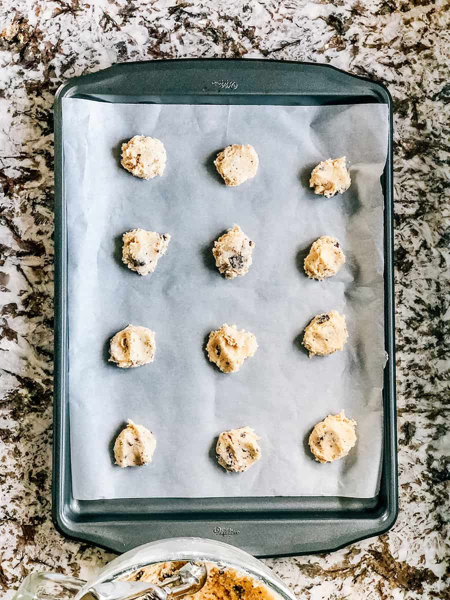 Boules de pâte d'une cuillère légèrement aplaties sur une plaque de cuisson recouverte de papier sulfurisé.