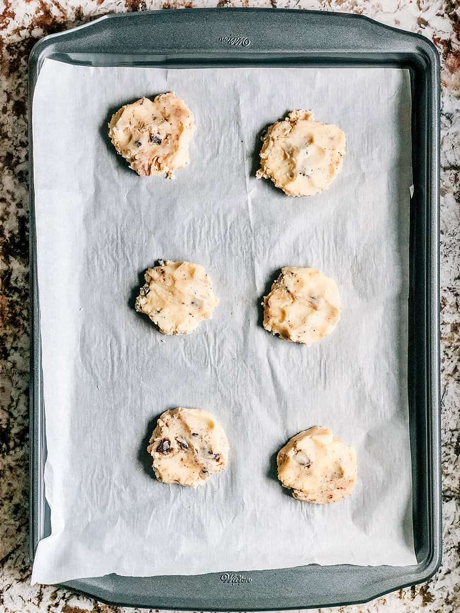 Boules de pâte de deux cuillères légèrement aplaties sur une plaque de cuisson recouverte de papier sulfurisé.