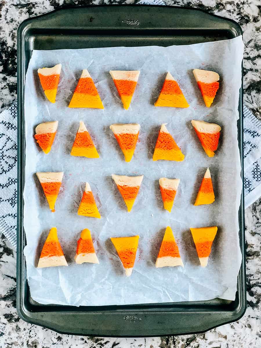 Une plaque de biscuits en forme de bonbons de maïs sur une plaque de cuisson tapissée de papier sulfurisé.