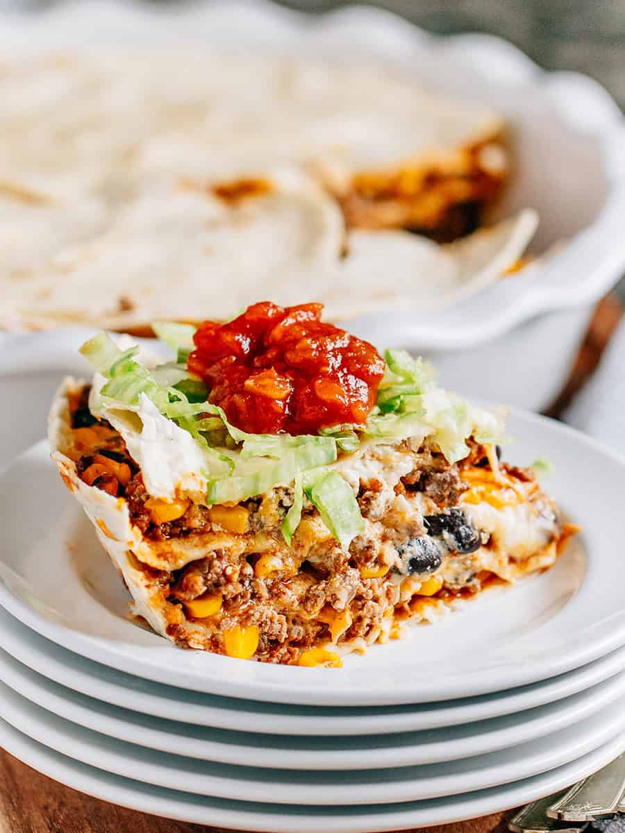 Une part de tarte taco montrant les couches de tortillas, viande de taco avec du maïs et des haricots noirs, crème aigre et fromage, puis garnie de laitue iceberg râpée et d'une cuillerée de salsa. Trop bon !