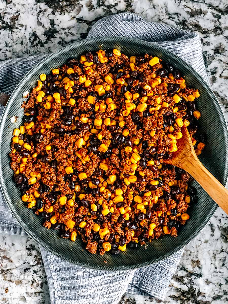 La poêle avec la viande hachée dorée transformée en viande à tacos mélangée avec le maïs en conserve et les haricots noirs égouttés et rincés.