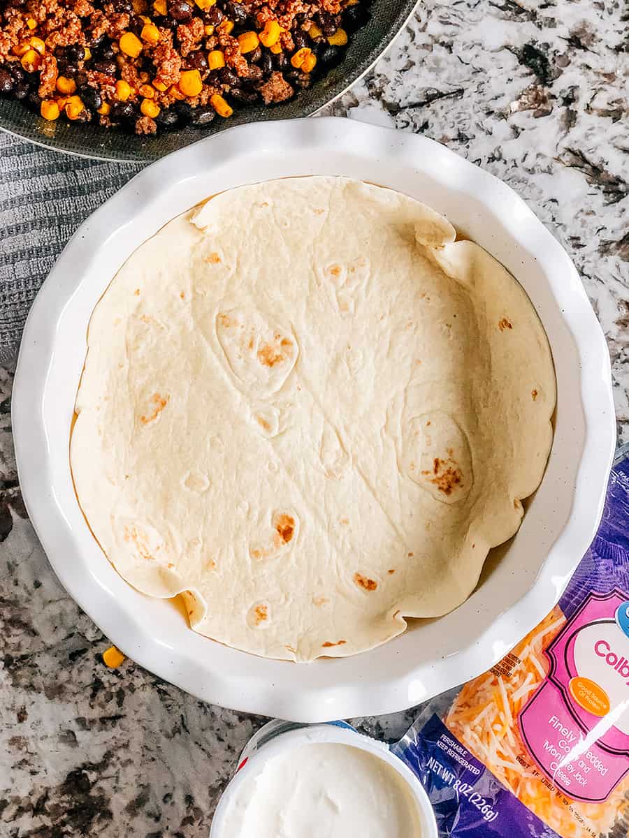 La première couche de la tarte taco consiste à former la tortilla de farine au fond du moule à tarte laissant l'excès de croûte monter sur le côté du moule.