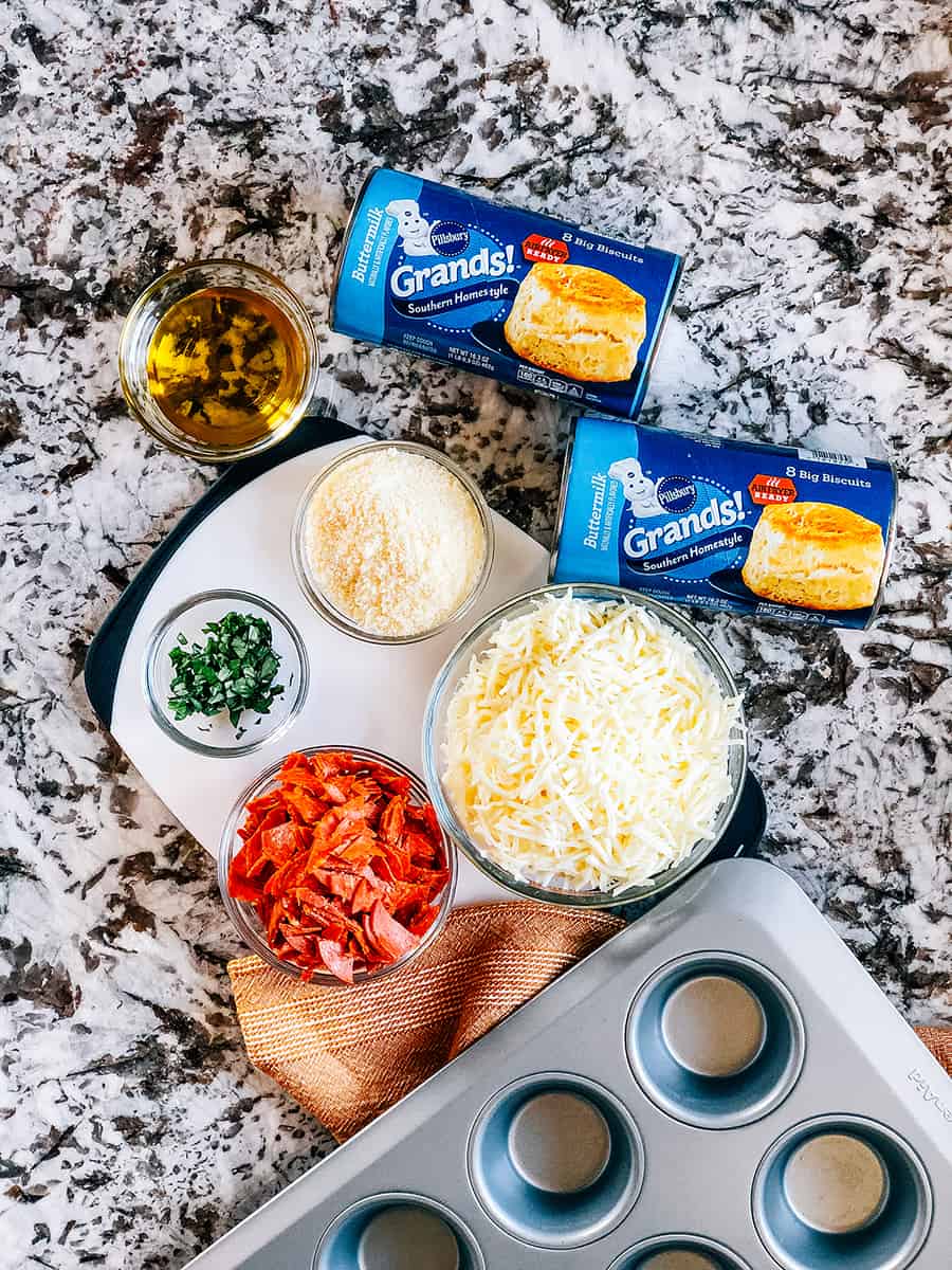 Les ingrédients pour les muffins à pizza à déchirer : biscuits Grands, huile d'olive, pepperoni, fromage mozzarella, basilic haché, et fromage parmesan.