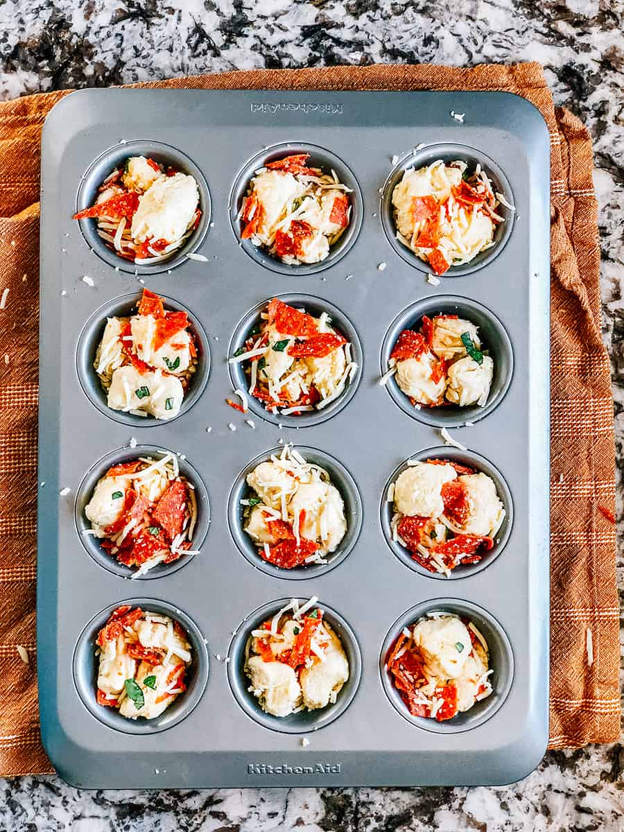 Le mélange de muffins à pizza avec beaucoup de fromage mozzarella et de pepperoni dans les moules à muffins.