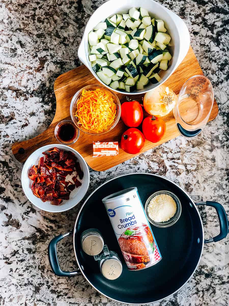 Les ingrédients pour le Zucchini à la Poêle : courgettes fraîches, tomates, oignons, fromage cheddar râpé, bacon émietté, beurre, sauce soja, chapelure et fromage parmesan râpé.