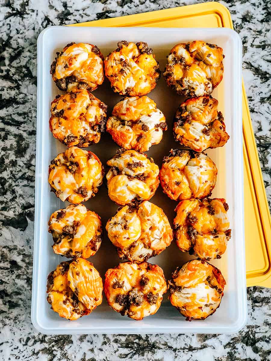 Des muffins au petit-déjeuner avec saucisse stockés dans un récipient Tupperware pour un petit-déjeuner facile à emporter.