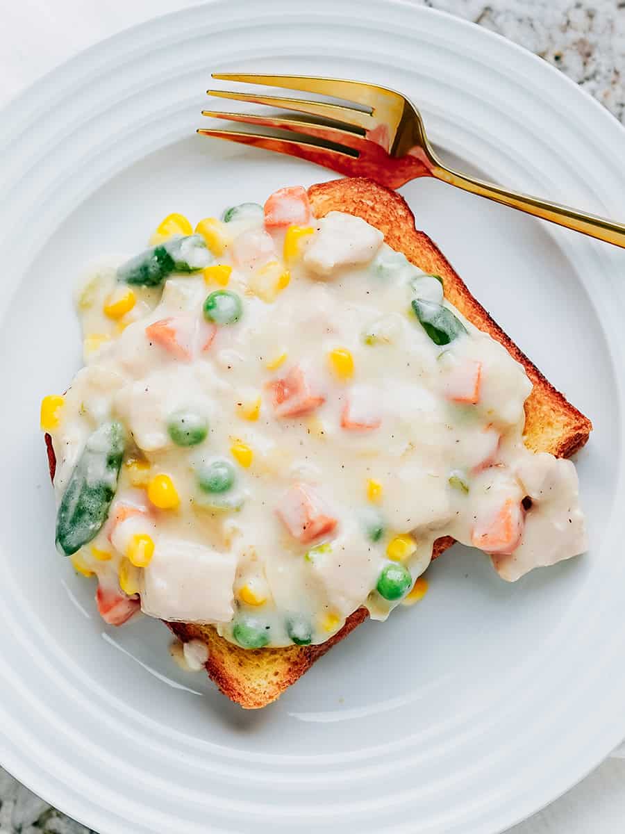 Une assiette avec de la dinde crémeuse et des légumes sur du pain brioche grillé.