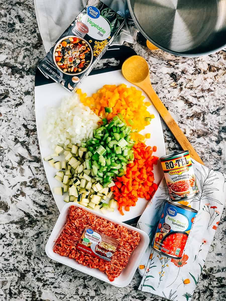 Aperçu des ingrédients de cette soupe de courgettes facile : cinq légumes en dés sur une planche à découper entourée d'un carton de bouillon de légumes, d'une boîte de Rotel et d'une boîte de tomates en dés petites.